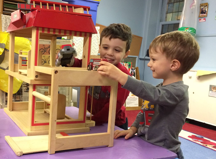 Two students play with a wooden firehouse