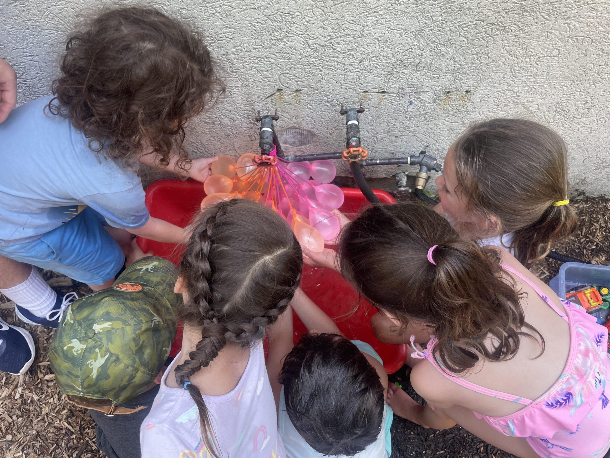 Students surround an outdoor faucet, making water balloons