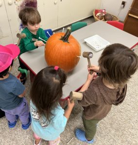 A group of students stands around a table hammering golf tees into a pumpkin